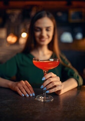 Smiling woman drinks coctail at the counter in bar