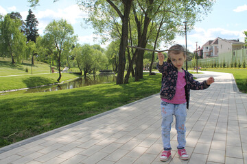 A little girl plays with a stick as with an airplane in a city park. The concept of a carefree happy childhood