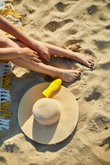 Top view Woman leg sitting on the sandy beach, near hat and sunscreen