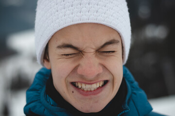 Candid portrait of a boy with a childish joyful smile in a winter white hat and blue jacket. Real...