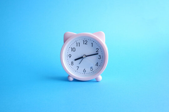 Cute pink alarm clock with cat's ears on bright blue background. Good morning or wake up concept. 