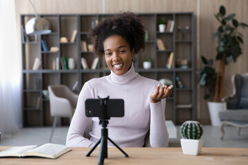 Smiling African American woman blogger influencer recording video on smartphone on tripod at...