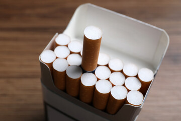Cigarettes with orange filters in pack on table, closeup