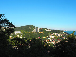 Obraz premium Southern city on a green hill by the sea under a blue sky.