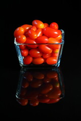 Fresh small red tomatoes in glass cup on dark background with reflex