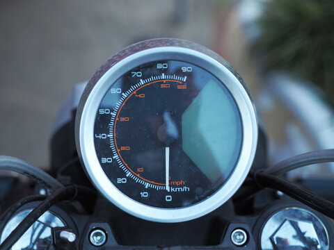 Round black spattered motorcycle speedometer. Front view. Closeup photo with blurred background