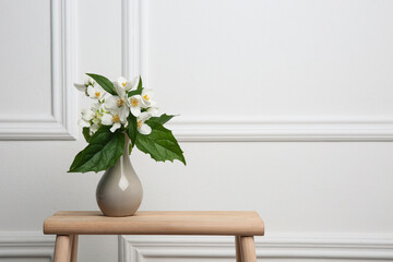 Beautiful bouquet with fresh jasmine flowers in vase on wooden table indoors, space for text