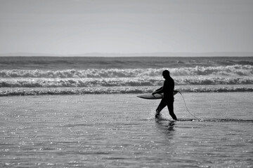 Surfers of all ages carry their surfboards to the water's edge of Llangennith beach on the Gower...