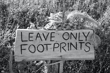 Leave only footprints. Monochrome photo of sign left for visitors at Llangennith Beach on the Gower Peninsula reminding them to leave take their litter home and leave no trace of them on the beach. 