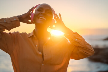 Happy senior African woman listening music in front of sea during summer sunset
