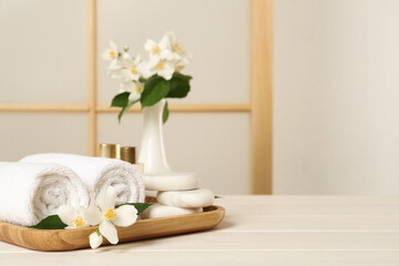 Obraz na płótnie Canvas Beautiful jasmine flowers, towels and spa stones on white wooden table, space for text