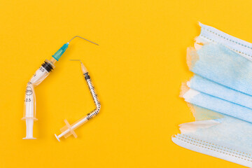 Anti Vaccine Movement and Anti Mask Concept - Broken Medical Syringe and Torn Medical Face Mask Lying on Yellow Background. Pandemic and Lockdown End - Top View, Flat Lay