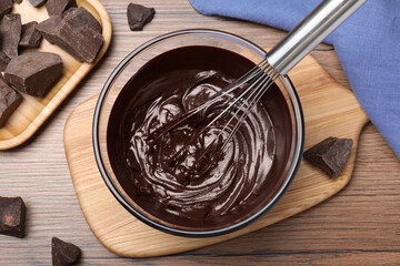 Delicious chocolate cream and whisk in glass bowl on wooden table, flat lay