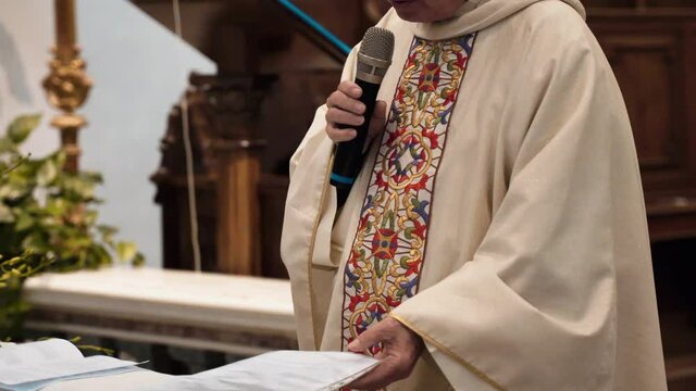 Italian local priest in beautiful ornamental clothes holding sermon in church reading from sheet paper and using microphone, senior pastor of traditional Italian church holding ritual ceremony sermon