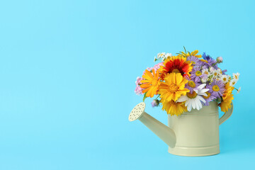 Yellow watering can with beautiful flowers on light blue background, space for text