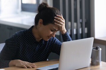 Unhappy Indian female employee upset about her mistake or problem with computer, getting bad news, suffering from headache. Tired frustrated woman working at laptop from home, feeling stress