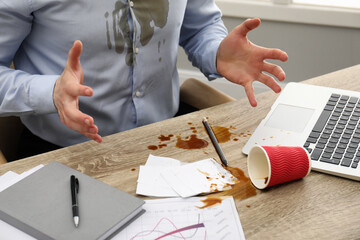 Man with spilled coffee over his workplace and shirt, closeup