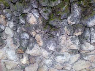 An old wall of stones of different sizes covered with moss. Photo