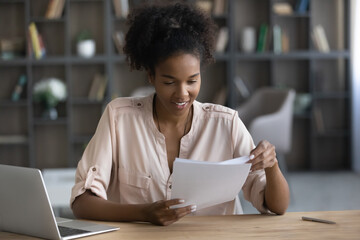 Smiling African American woman working with documents, sitting at desk, positive freelancer or...