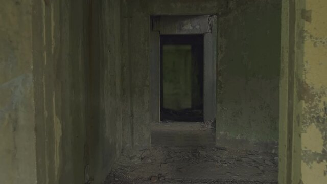 Walking along dark long corridor in abandoned building with shabby walls.