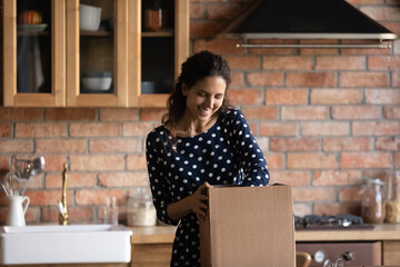 Happy woman unpacking carton box in kitchen, opening package, producing goods from paper container,...