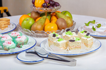 Plates with different cakes. Cake tongs. A bowl of fruit.