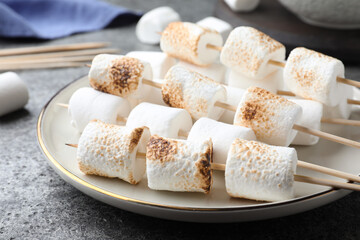 Sticks with roasted marshmallows on grey table, closeup