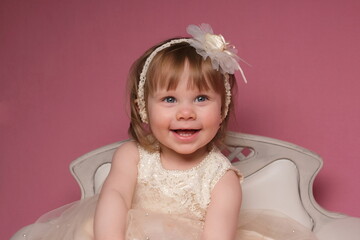 Children's studio photo session on a pink background A girl sits in a beige dress on a white sofa