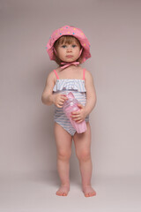 A girl in a striped swimsuit and a pink hat stands on a white background and holds a cocktail in her hands