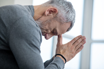 A gray-haired man sitting with eyes closed and saying the payers