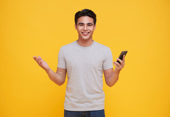 Happy handsome Asian man celebrating with mobile phone isolated over yellow background.