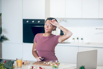 A dark-skinned woman cooking in the kitchen while watching a cookery vlog