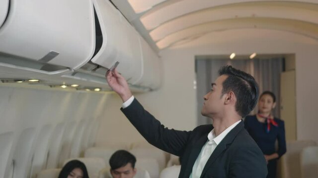Flight attendant woman service helping businessman passenger to put luggage suitcase cabin compartment on airplane