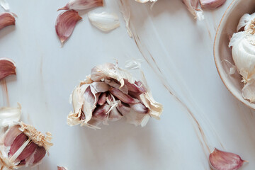 Purple garlic cloves opened on a marble table and bowl with parts of garlic