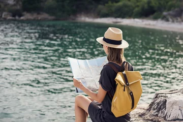 Foto op Canvas Young woman traveler with backpack holding map by the sea. Travel, tourism, summer holidays, active lifestyle, enjoying life concept. Beautiful tourist girl looking for hiking route  © kite_rin