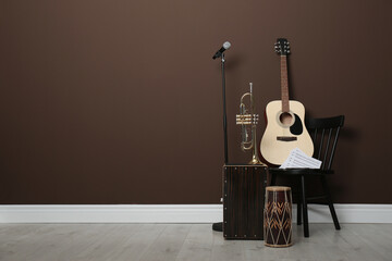Acoustic guitar, trumpet, hand drum and microphone near brown wall indoors, space for text. Musical...
