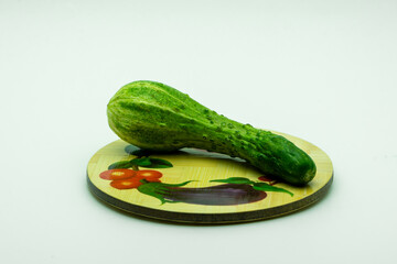 Fresh deformed green cucumber lies on a rustic plate on the white background. The natural vegetable is good for diet because it contains many vitamins and microelements. Horizontal copy space image.