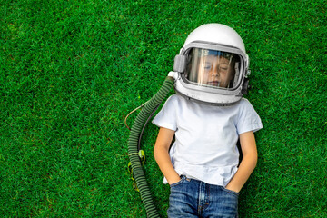 A child lies on the grass wearing an astronaut's helmet and dreams of great achievements!