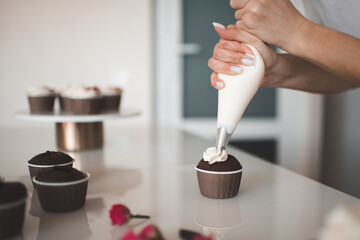 Woman decorate  homemade creamy chocolate cup cakes with cream stay on kitchen table close up....