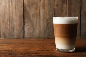 Glass of delicious layered coffee on wooden table, space for text