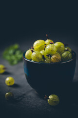 Fresh ripe berries of green gooseberry in a blue bowl on dark gray background. Selective focus.