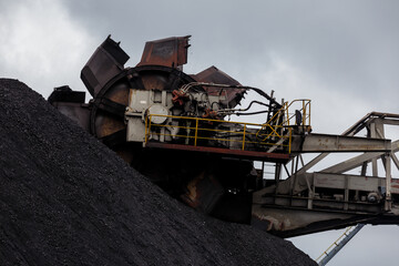 Open-air coal terminal. Close-up. The spinning bucket is hovering over the coal heap.