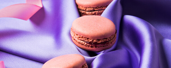 Pastel pink french macaroons on purple silk fabric background