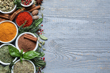Different natural spices and herbs on grey wooden table, flat lay. Space for text