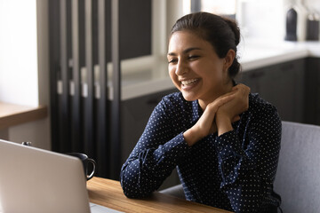Happy Indian female employee working at laptop from home, attending virtual meeting or conference,...
