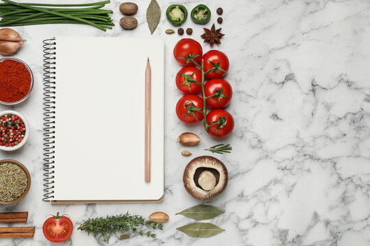 Open recipe book and different ingredients on white marble table, flat lay. Space for text