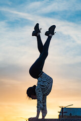 Silhouette of flexible woman gymnast doing handstand on the dramatic sunset. Concept of willpower, motivation and passion