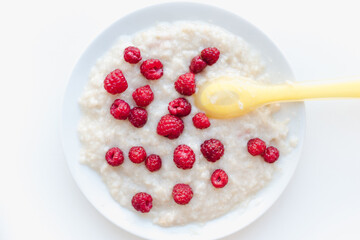 porridge with berries on a white plate, oatmeal with raspberries, baby porridge 