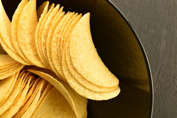 Several potato chips in a black ceramic plate, close-up, top view.