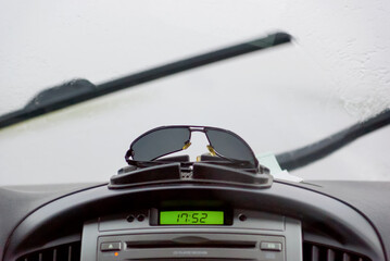 sunglasses on the car panel on the background of the windshield and wipers - obrazy, fototapety, plakaty